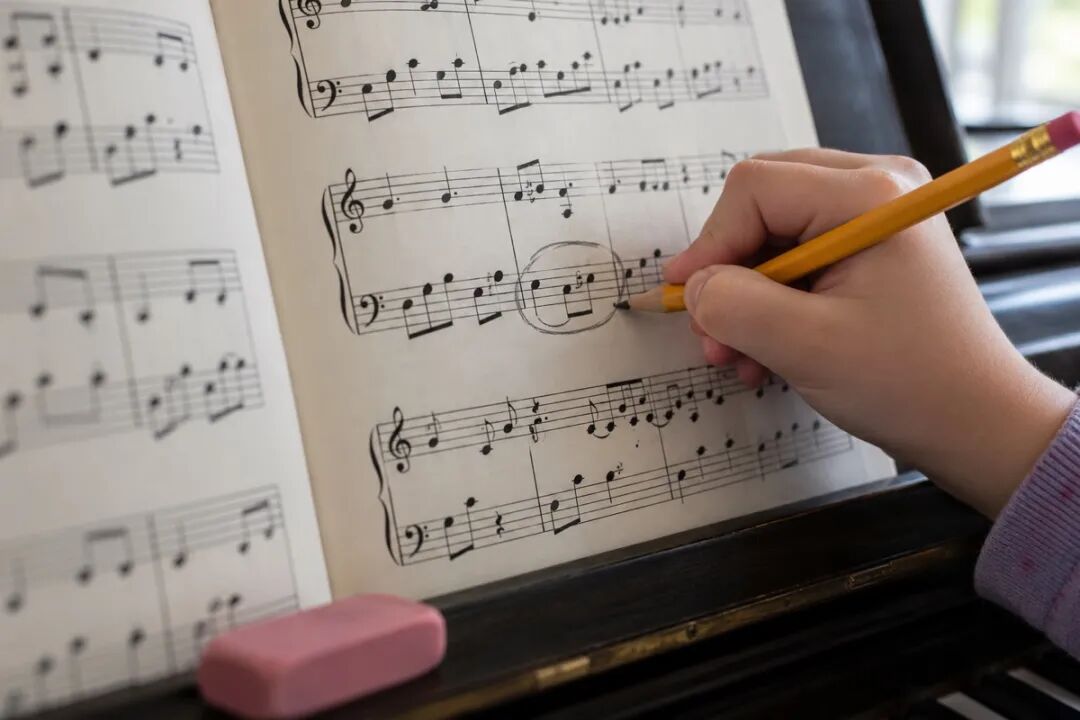 孩子的手握着黄色铅笔,在钢琴谱低音谱表的一个小节外画圈,示意下课后自己把老师指出的地方圈出来。